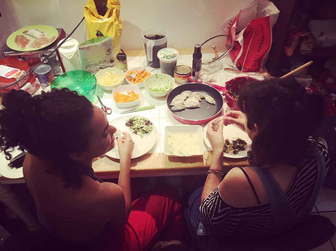 Two friends smile at each other while making dumplings